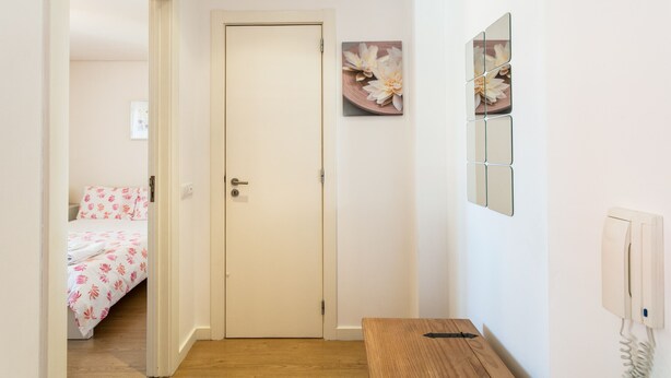 Habitació d'hotel amb terra de fusta, un llit amb edredó floral, una porta blanca, un telèfon fixat a la paret i un quadre amb flors.