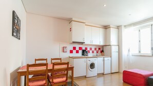 Una cuina compacta amb zona de menjador, una rentadora i un pouf vermell.