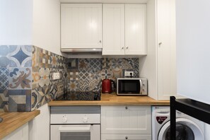 A compact kitchen with white cabinets, a microwave, a red kettle, and a washing machine.