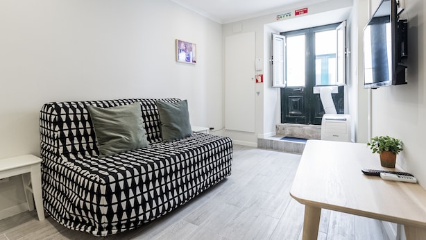 Una habitación moderna con un sofá estampado, una mesita, un televisor y una puerta que da a un baño.