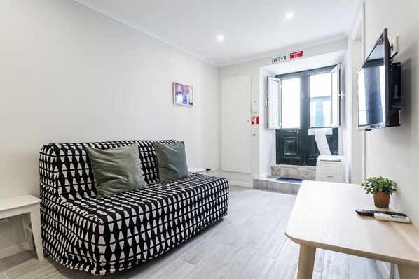 A modern room with a patterned sofa, a small table, a TV, and a door leading to a bathroom.