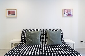 A bed with a black and white geometric pattern, two pillows, a white nightstand, and two framed pictures on the wall.