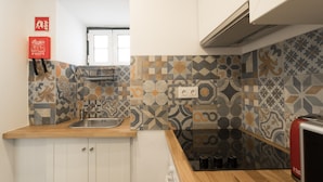 Una cocina con baldosas estampadas, encimera de madera, un lavamanos, armarios y un electrodoméstico rojo.