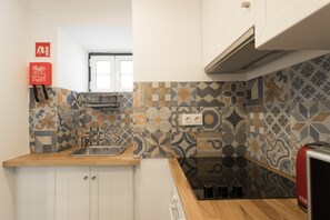A kitchen with patterned tiles, a wooden countertop, a sink, cabinets, and a red appliance.