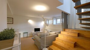 Una sala de estar moderna con una escalera de madera, un sofá, una lámpara de pie y un televisor.