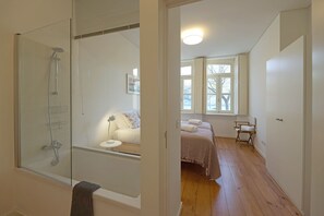 A bathroom with a glass-enclosed shower, a white bathtub, and a wooden floor.