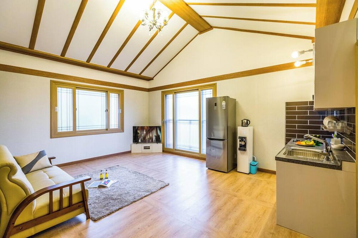 A spacious living area with a sofa, a TV, a refrigerator, and a kitchen area with a sink and countertop.