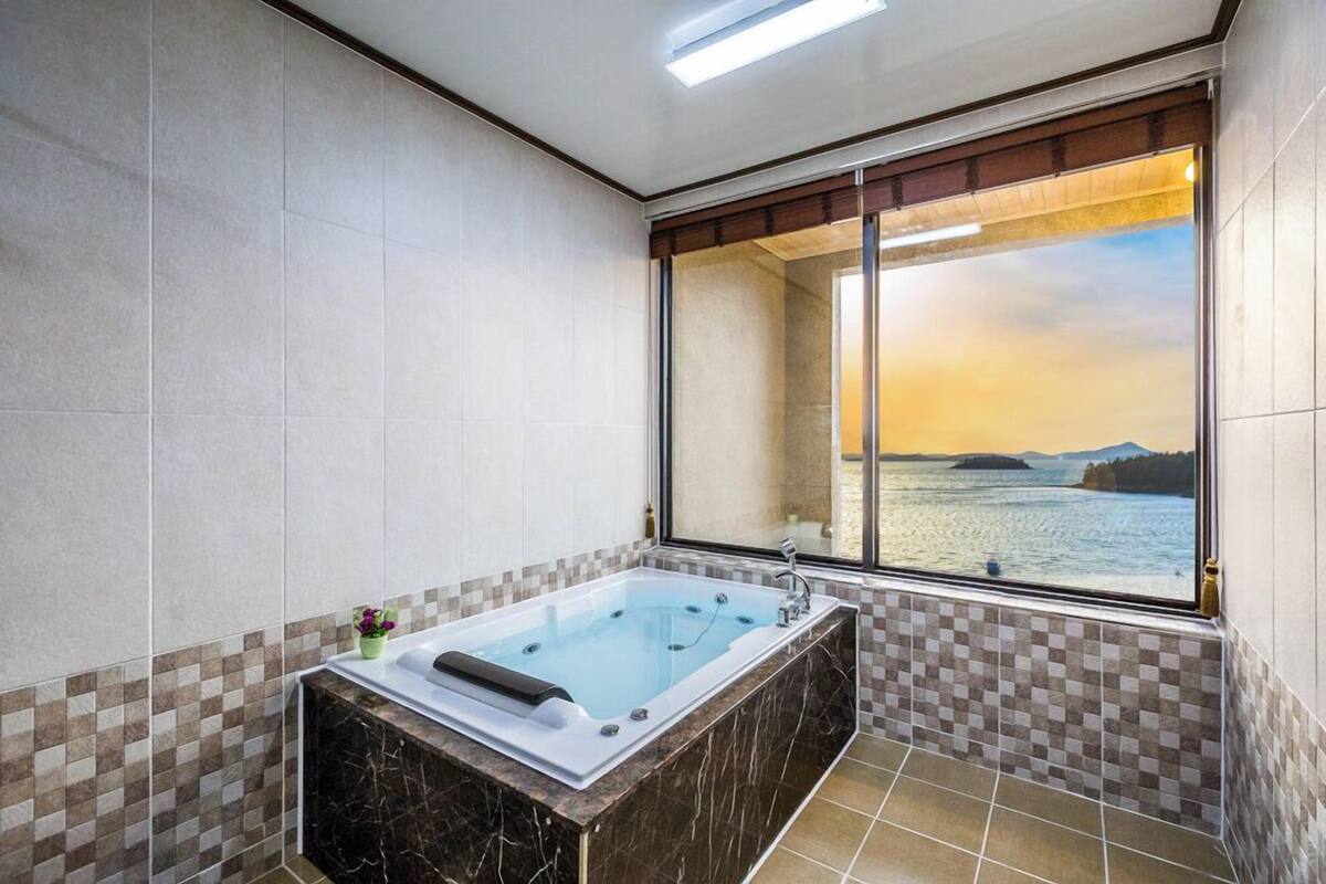 A modern bathroom with a large bathtub, checkered tiles, and a view of a body of water through a large window.