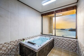 A modern bathroom with a large bathtub, checkered tiles, and a view of a body of water through a large window.