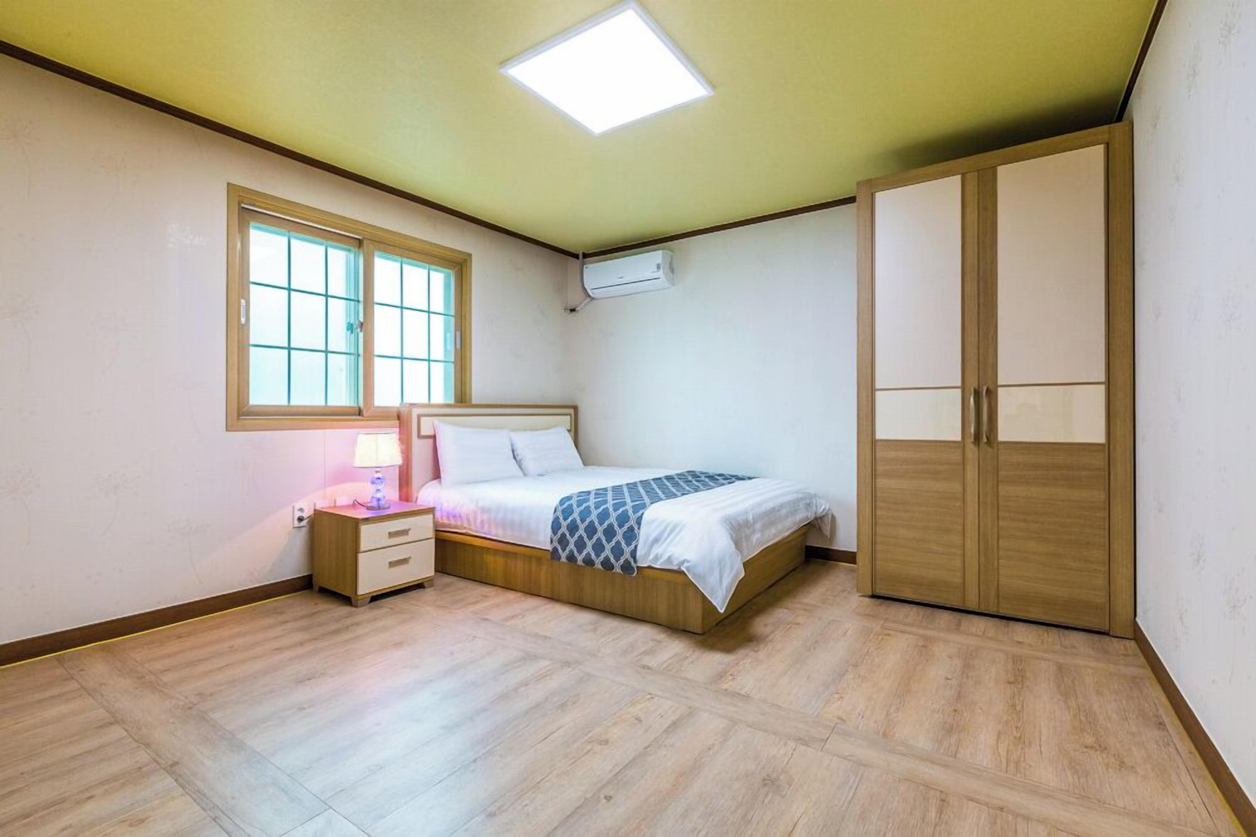 A bedroom with a bed, bedside table, lamp, wardrobe, window, and ceiling light.