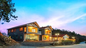 A modern two-story building with large windows and a balcony, surrounded by a natural landscape. - Hue travel Pension (Muan)
