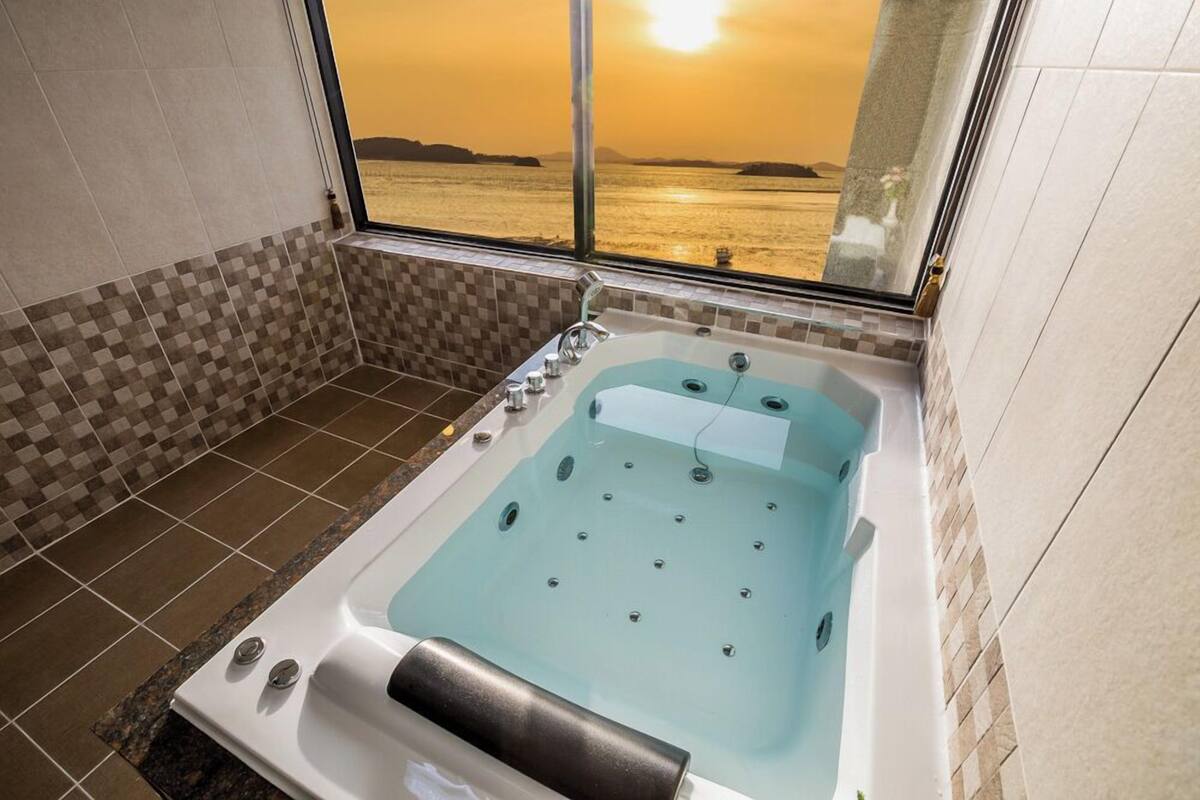 A bathroom with a large bathtub, a window with a view of the sea, and tiled walls.