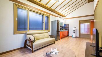 A living room with a sofa, a coffee table, a television, and a kitchen area with a refrigerator and cabinets.