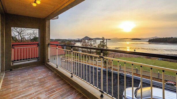 A balcony with a view of a sunset over a body of water, a vehicle, and a distant mountain range. - Hue travel Pension (Muan)
