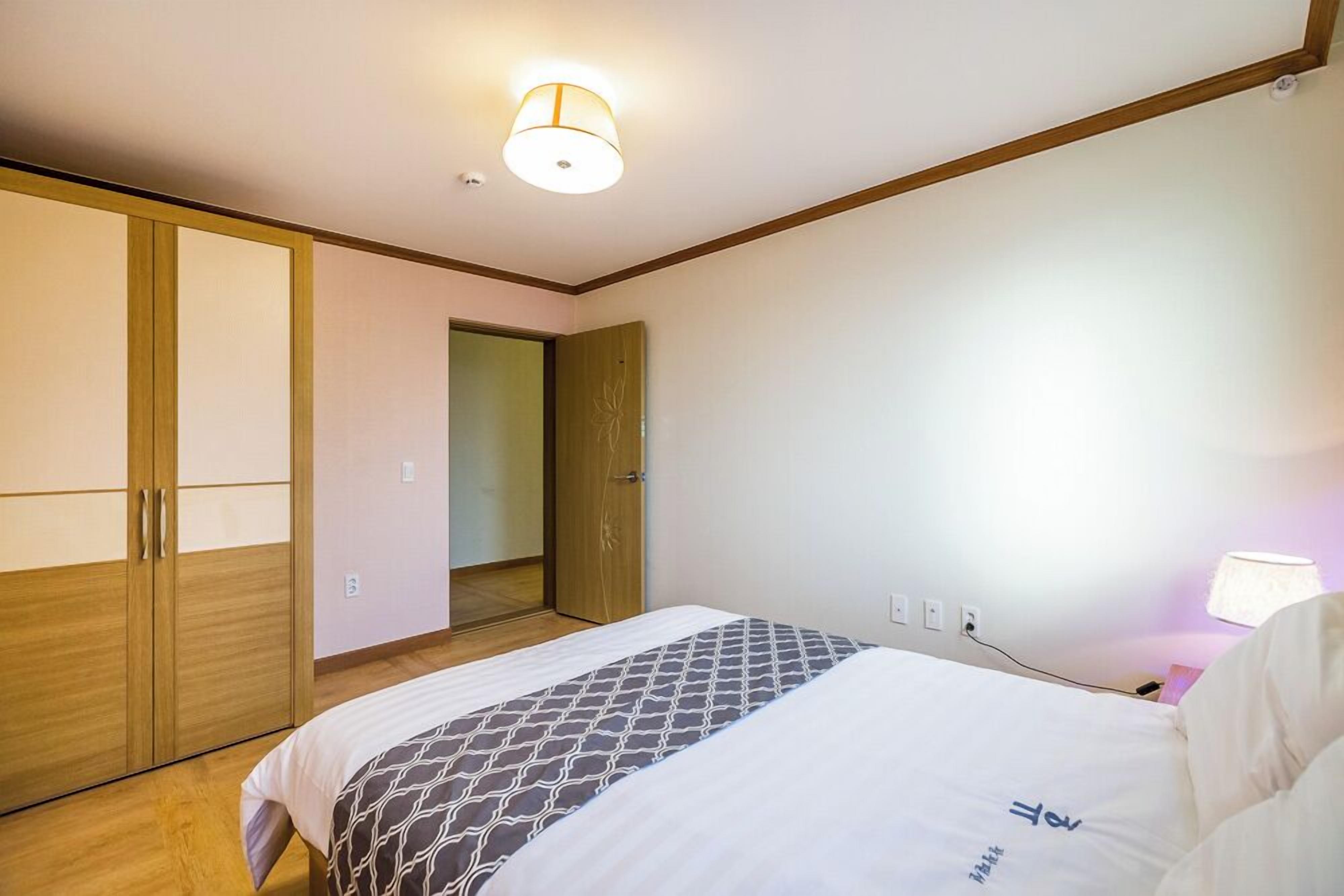 A hotel room with a bed, a wardrobe, a bedside table with a lamp, and a ceiling light.