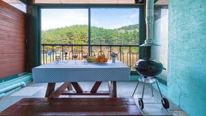 Un balcón con una mesa dispuesta para una comida, una parrilla y vistas a un paisaje verde.
