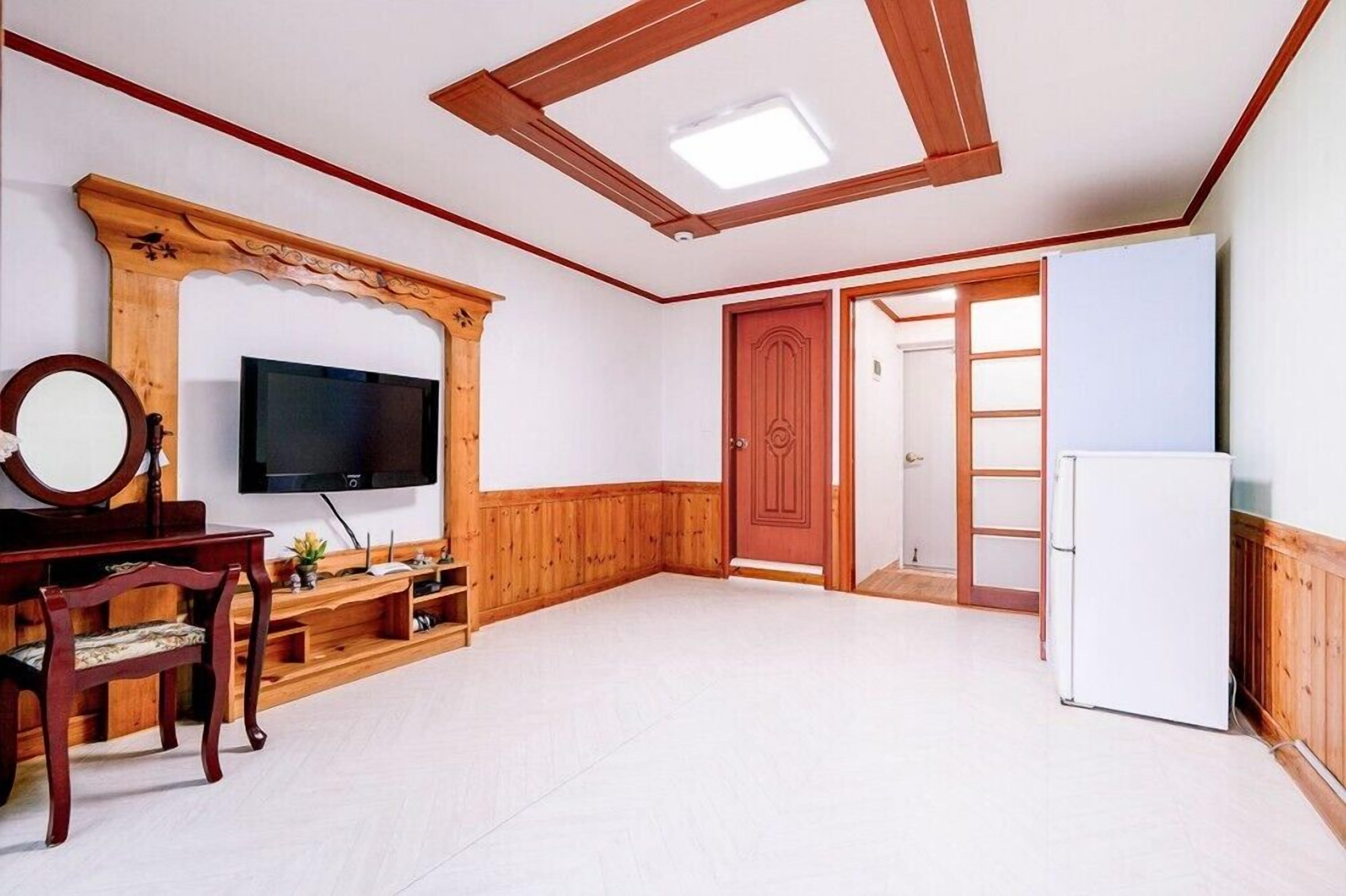 A room with a wooden TV stand, a flat-screen TV, a wooden door, and a white refrigerator.