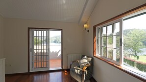 A room with a large window, a chair with a cushion, and a view of a balcony and greenery.