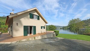 A two-story house with green shutters, a paved driveway, and a view of a river.