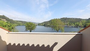 A balcony with a view of a lake surrounded by greenery and hills.