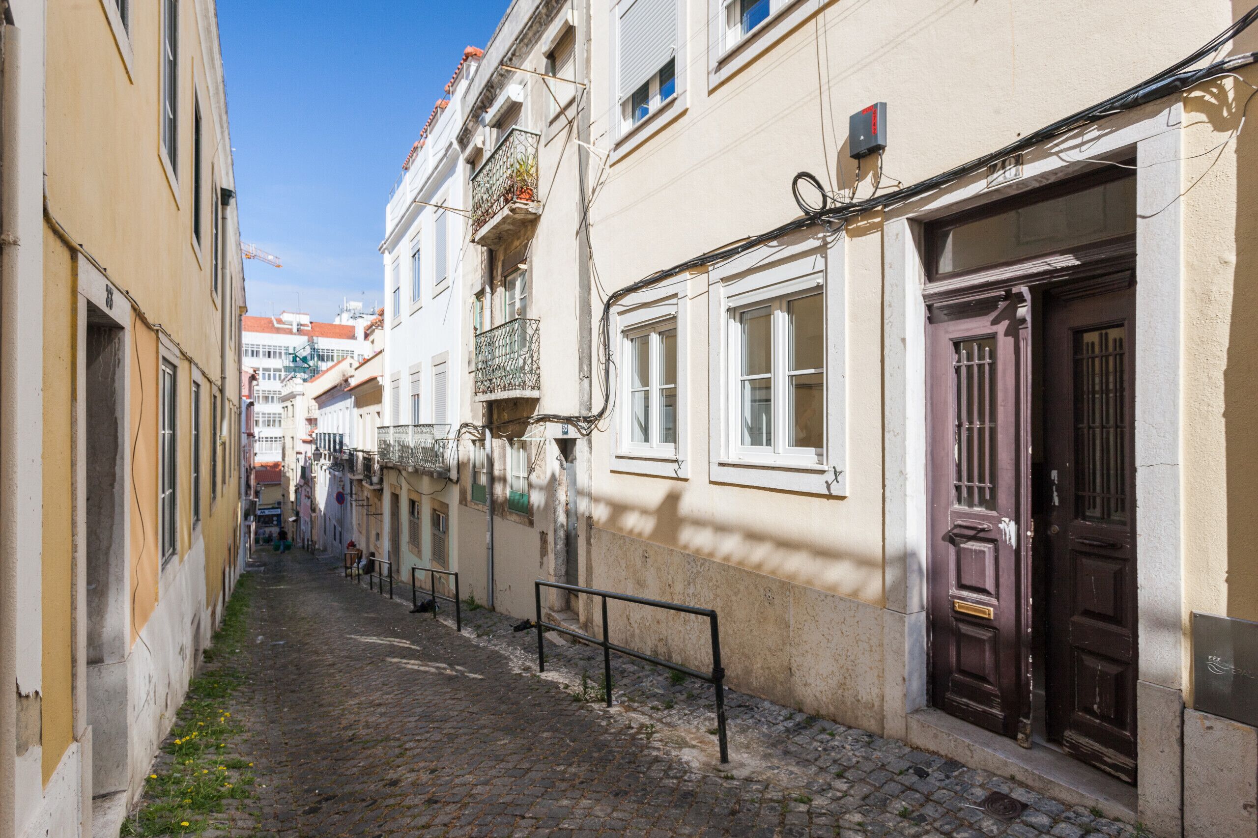 A narrow cobblestone street lined with historic buildings, featuring balconies, wooden doors, and a clear blue sky.