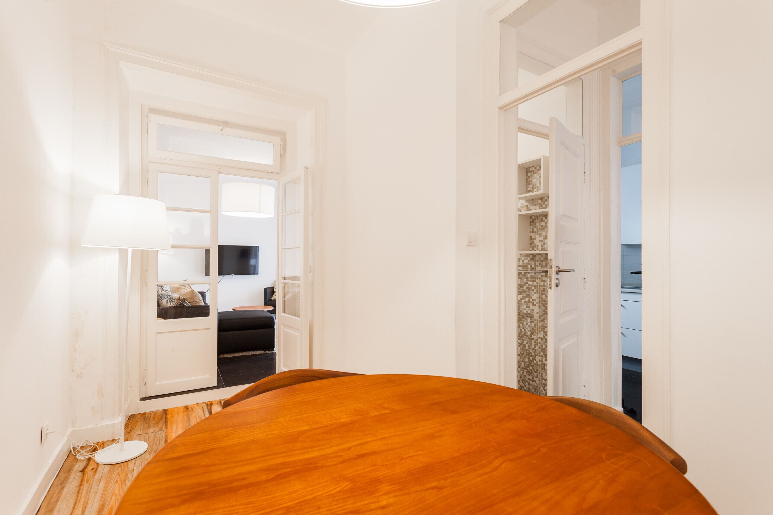 A room with a wooden table, a lamp, and a door leading to a balcony.