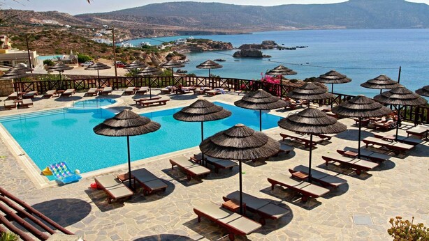 Zwembadgedeelte van een resort met ligbedden en parasols, met uitzicht op een kustlandschap.