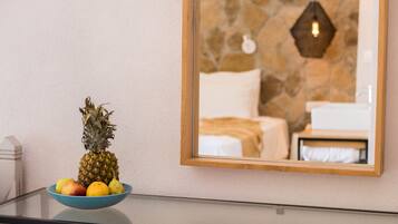 Una ciotola di frutta con ananas e mele su un tavolo di vetro, uno specchio con cornice in legno che riflette un muro in pietra e un letto.