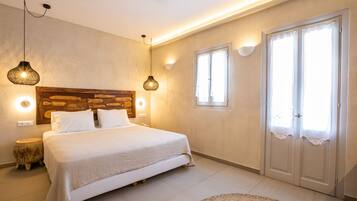 Une chambre avec une tête de lit en bois, un lit avec une literie blanche, deux lampes suspendues, un tapis rond et une porte double avec des rideaux.