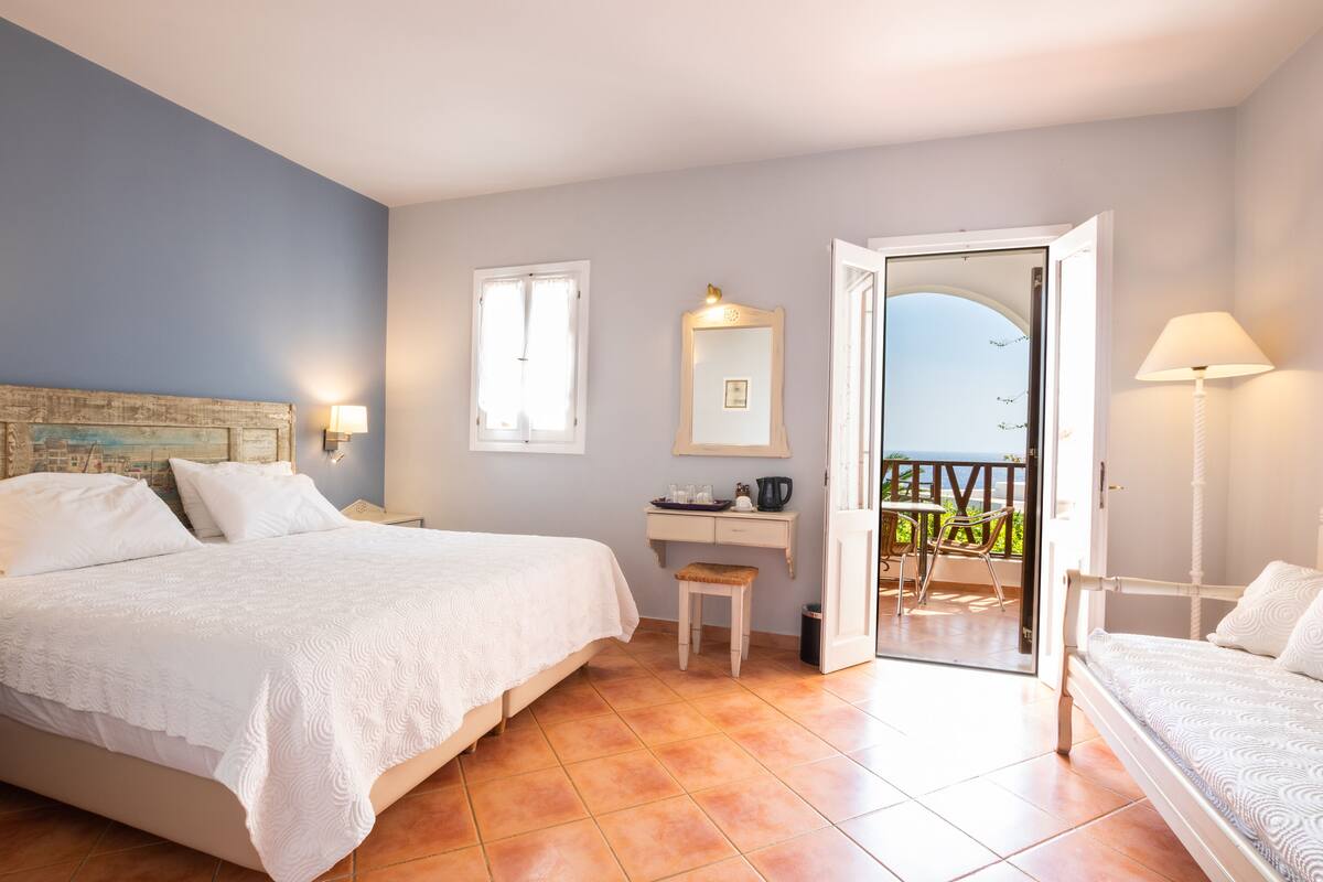 A bedroom with a bed, a desk, and a balcony with a view.