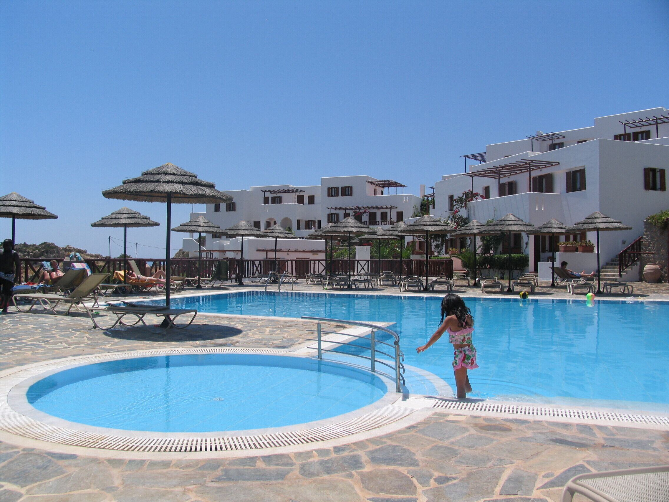 A swimming pool with lounge chairs and umbrellas, surrounded by white buildings with balconies.