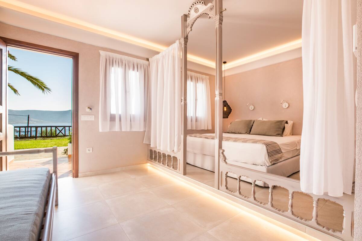 A bedroom with a large mirror, a bed, a view of the outdoors, and a balcony.