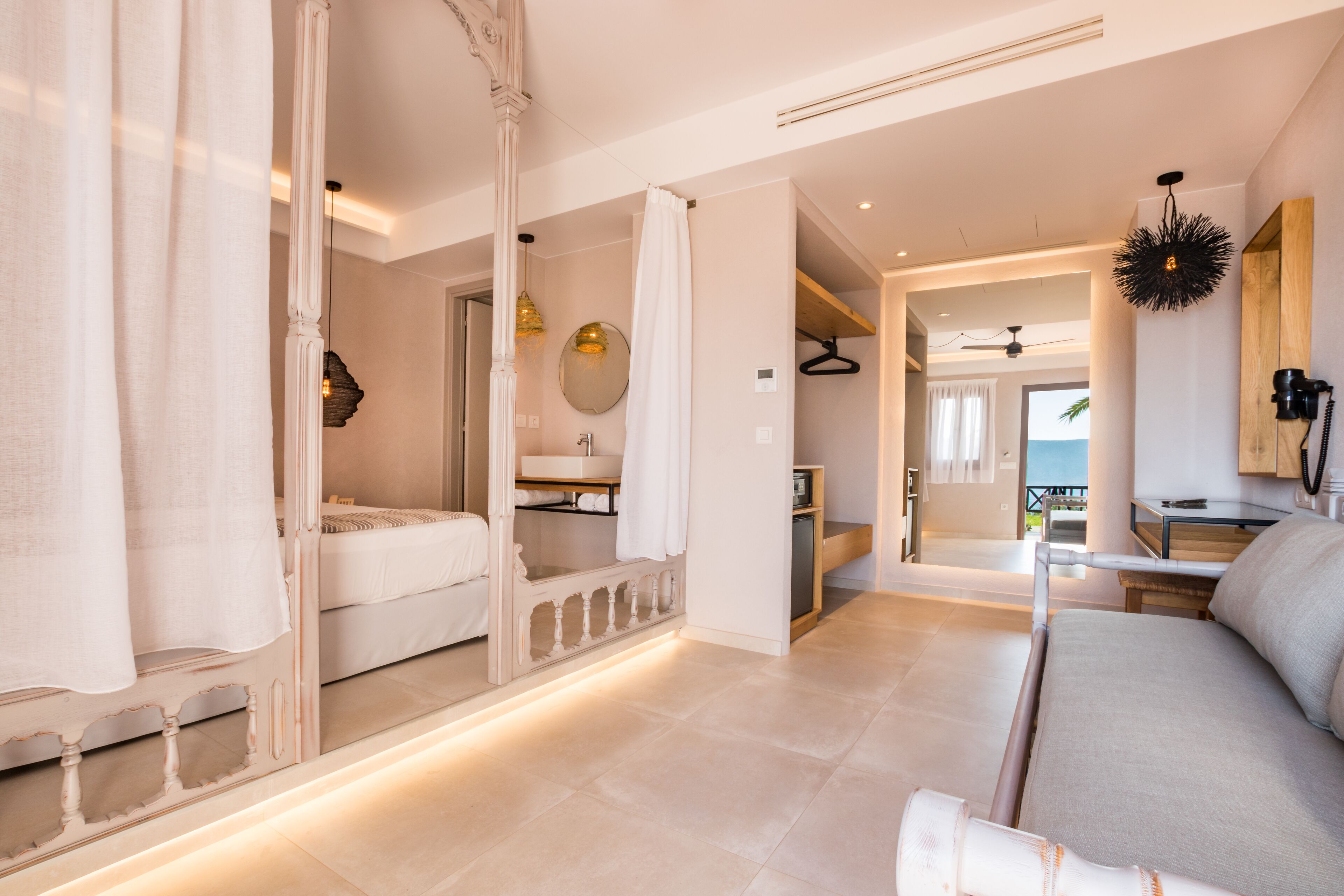 A modern hotel room with a large bed, a sitting area, and a bathroom with a mirror and sink.
