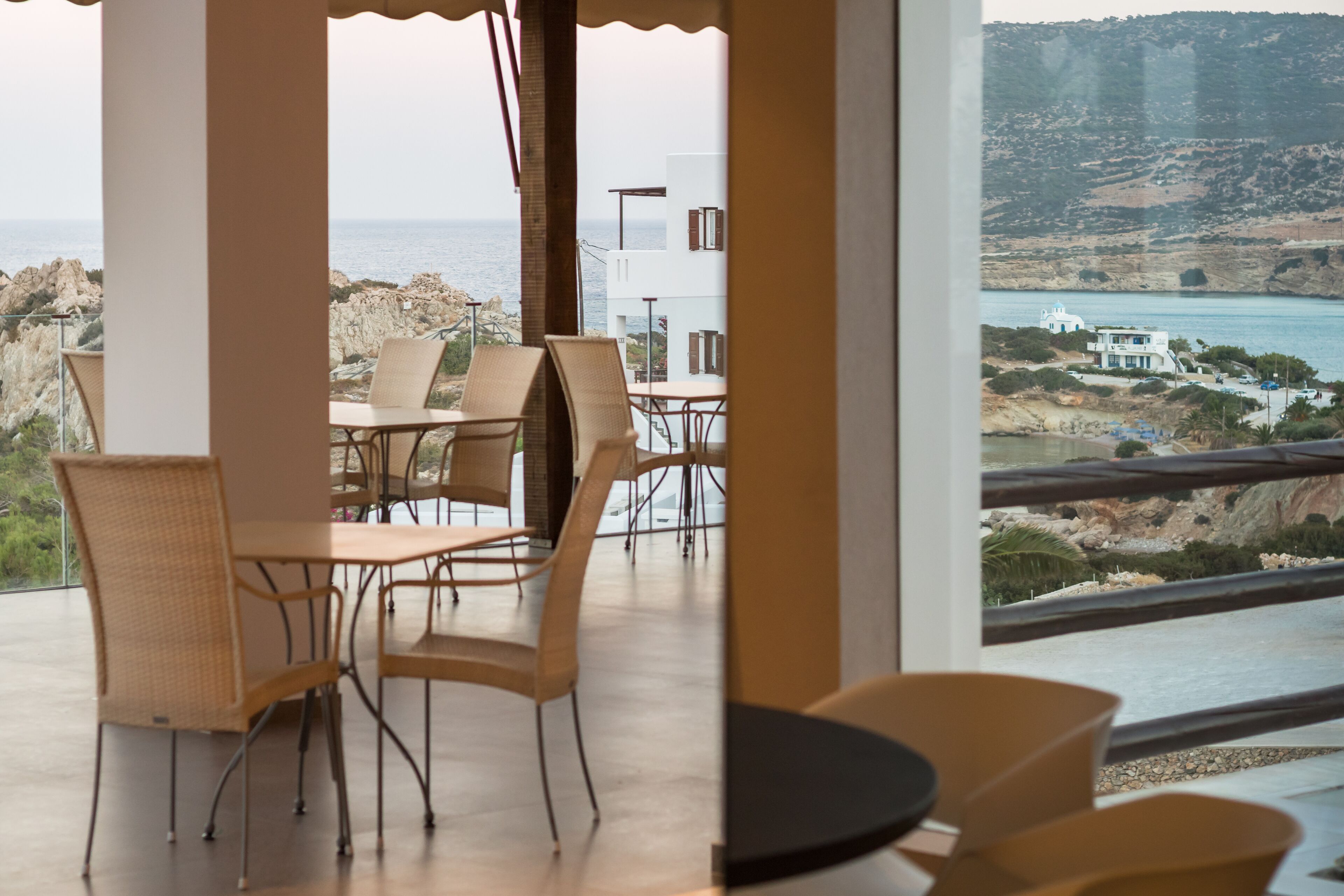 A dining area with wicker chairs and a table, overlooking a coastal landscape with buildings and cliffs.