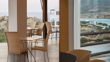 A dining area with wicker chairs and a table, overlooking a coastal landscape with buildings and cliffs.
