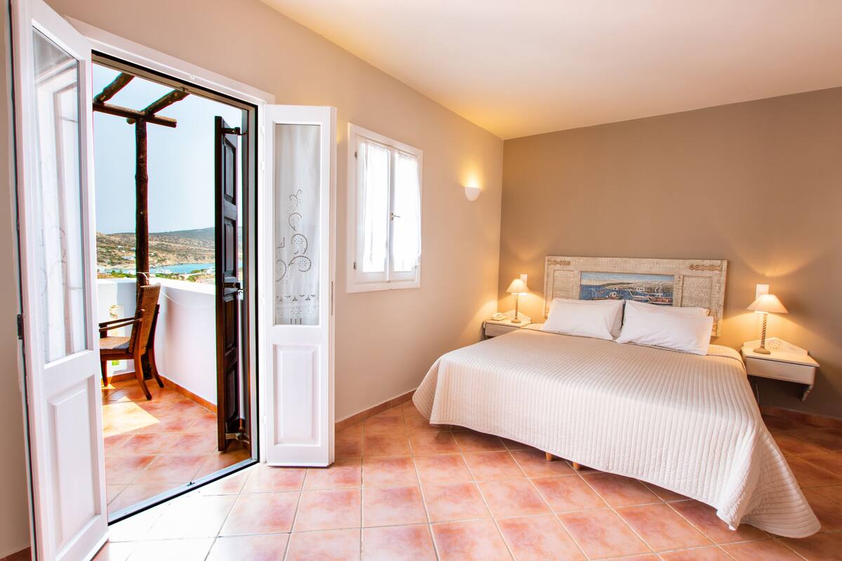 A bedroom with a bed, two bedside lamps, a nightstand, a window with curtains, and a view of the outdoors.