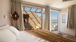 Een slaapkamer met een groot bed, uitzicht op de omgeving, een stenen muur en een plafondventilator.