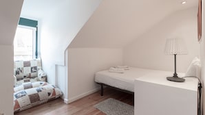 A bedroom with a bed, a bedside lamp, a window, a patchwork sofa, and a wooden floor. - FLH Lx Factory Modern Flat (Lisbon)
