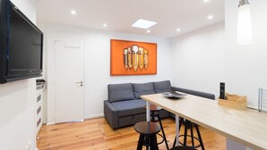 A modern room with a sofa, a dining table, a TV, and a painting on the wall. - FLH Lx Factory Modern Flat (Lisbon)