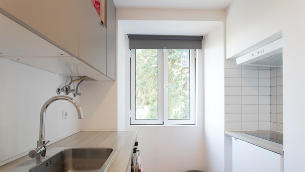 A kitchen with a stainless steel sink, a window with a blind, and a trash bin. - FLH Lx Factory Modern Flat (Lisbon)
