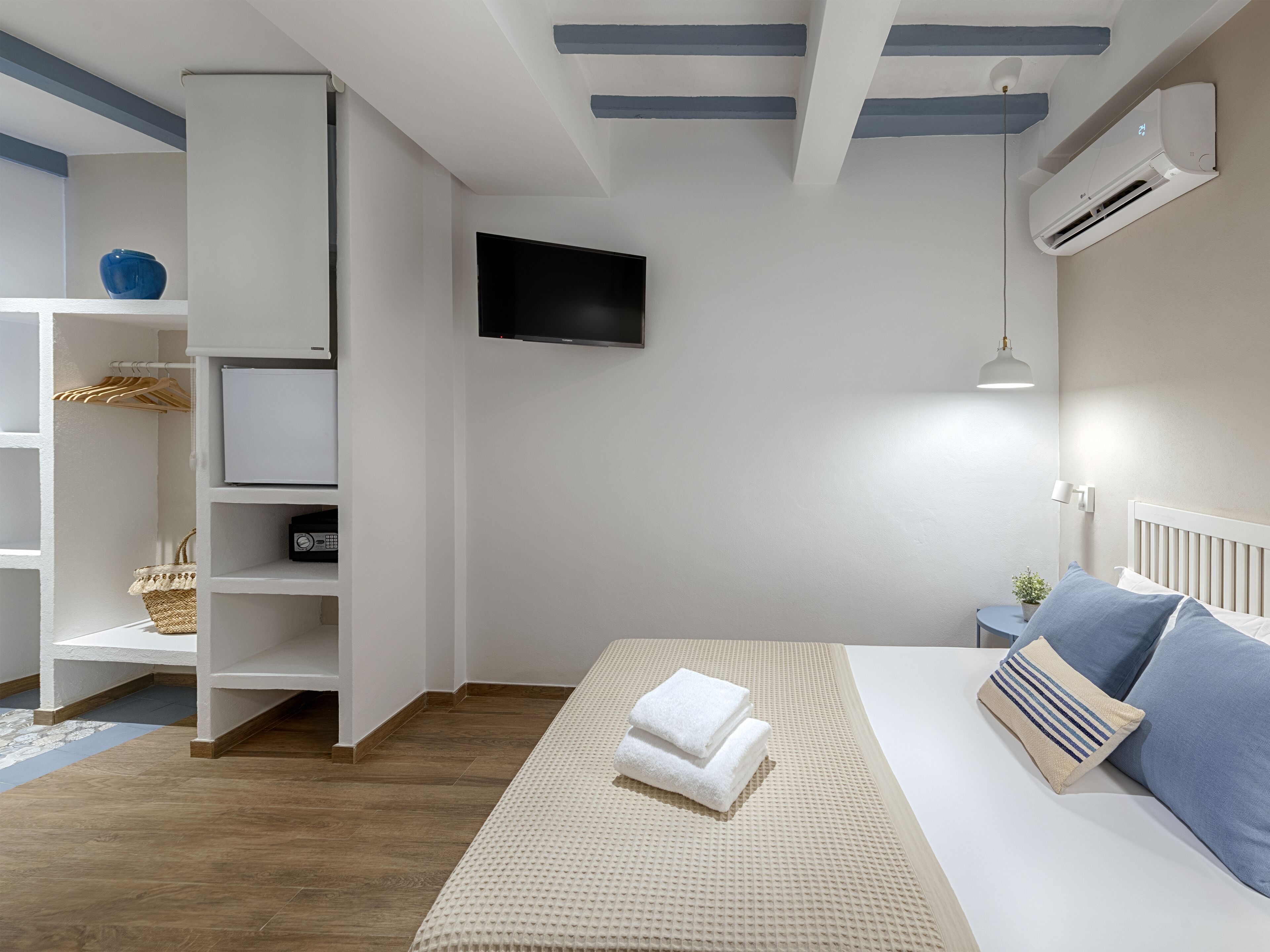A modern bedroom with a bed, a TV mounted on the wall, and an air conditioning unit.