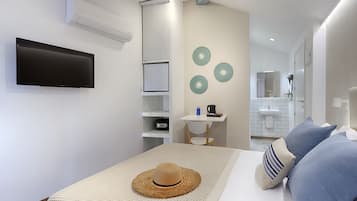 Una habitación de hotel moderna con una televisión de pantalla plana, un escritorio pequeño con una silla, una cama con almohadas azules y a rayas, y un aire acondicionado instalado en la pared.