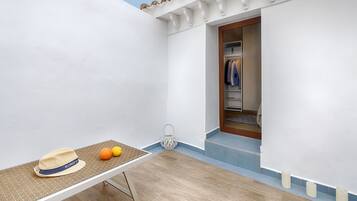 Une pièce avec une table, un chapeau et des oranges. Il y a une porte qui donne sur un placard rempli de vêtements.