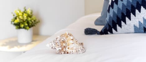 Un lit avec un oreiller à motifs, un coquillage et une petite plante en pot sur une table de chevet.