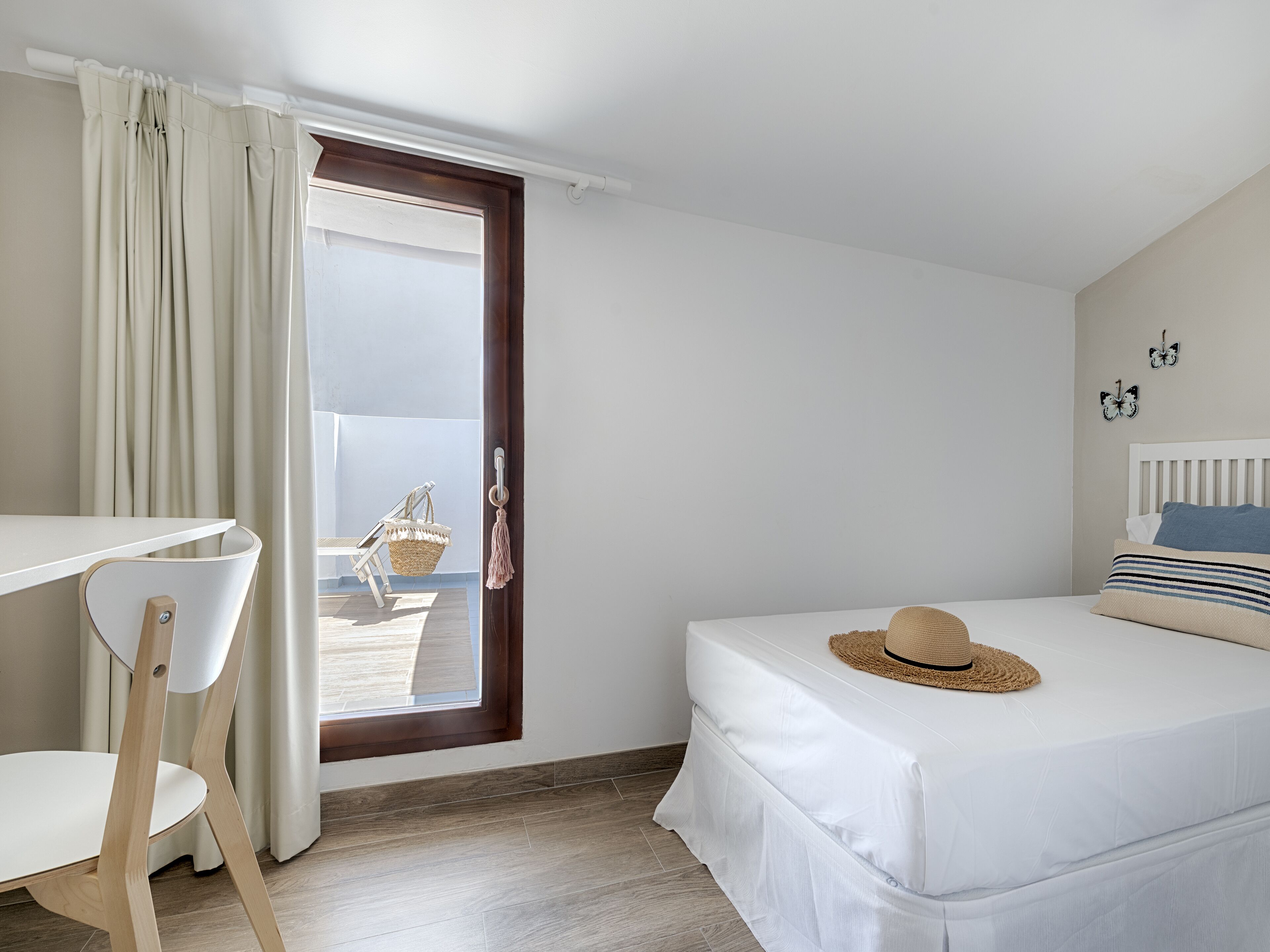 Une chambre à coucher comprenant un lit, une chaise, une petite table, une fenêtre avec des rideaux et une vue sur l’extérieur.