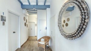 A hallway with a wooden floor, a wicker chair, and a decorative mirror on the wall. - Hostal Altea House (Altea)