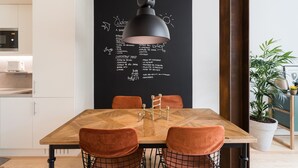 Un espace de salle à manger moderne avec une table en bois, des chaises orange et un luminaire suspendu noir.