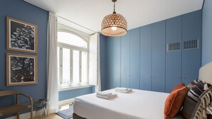 Une chambre à coucher avec un lit, une chaise, une fenêtre et un mur orné de deux tableaux encadrés.