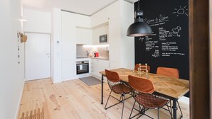 Une cuisine moderne avec des meubles blancs, une table à manger en bois et des chaises orange, ainsi qu’un mur noir où sont énumérés les principaux sites touristiques de la région.