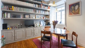 A dining area with a wooden table and chairs, surrounded by bookshelves filled with books and decorative items. - FLH Janelas Verdes Charming Flat (Lisbon)